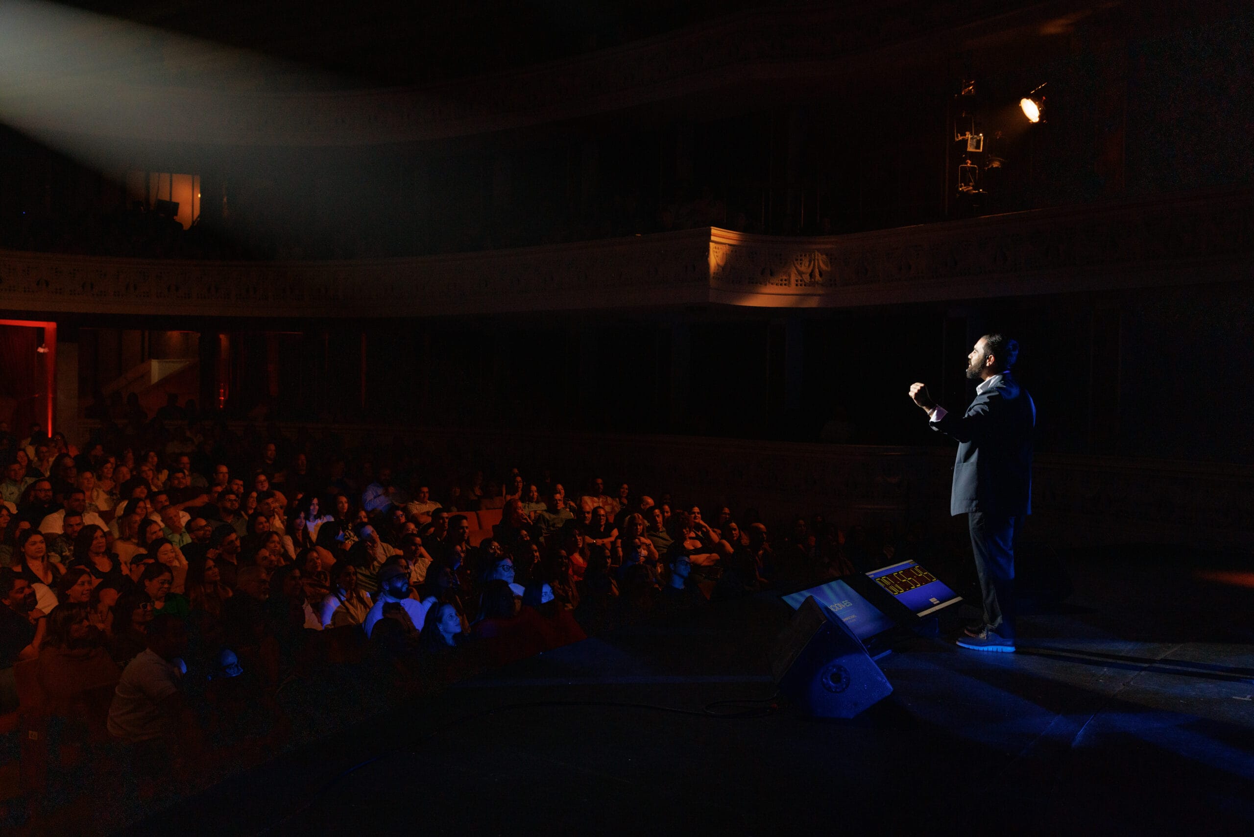 Orador en un escenario de teatro frente a una audiencia.